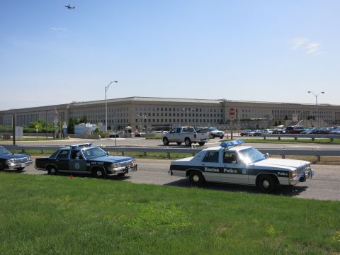 1991 Ford LTD Crown Victoria - State Police cruiser and Boston Police cruiser sit before a long government building as an aircraft flies overhead.