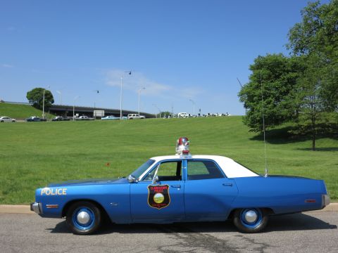 1991 Ford LTD Crown Victoria - blue sedan with white roof marked POLICE, fitted with a roof light and tall antenna, sits in profile on a grassy field.