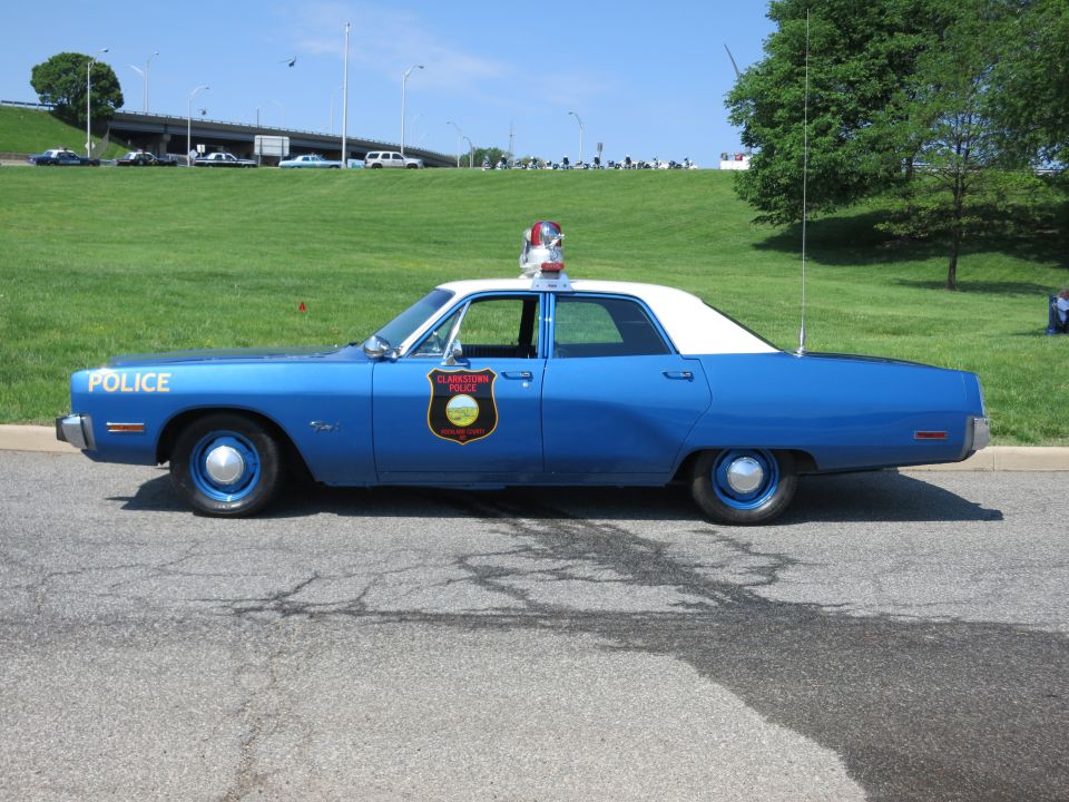 Blue Police sedan with white roof, shield decal and roof light, side profile on pavement