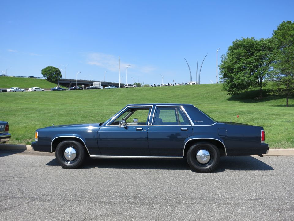Dark blue four-door sedan, driver-side profile, parked on pavement by a grassy slope