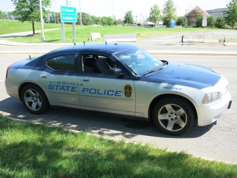 1991 Ford LTD Crown Victoria - silver Dodge Charger lettered 'Virginia State Police Trooper' parked along a road near green highway signage.