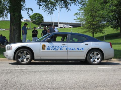 1991 Ford LTD Crown Victoria - silver 'Virginia State Police' Dodge Charger parked on a street, with people and a highway overpass in the background.