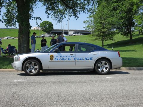 1991 Ford LTD Crown Victoria - silver 'Virginia State Police' Dodge Charger parked in profile under trees, with spectators and a highway overpass behind.