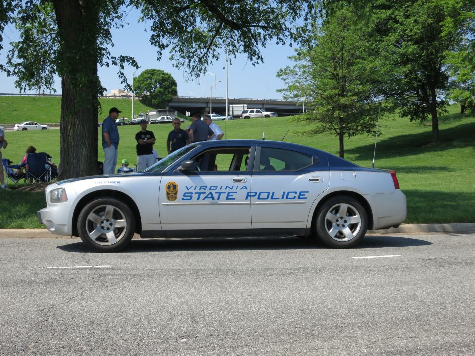 Silver Virginia State Police Dodge Charger in profile by trees and overpass