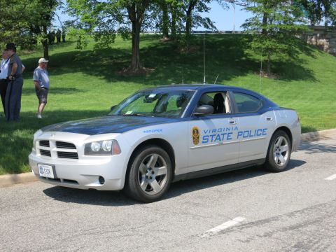 1991 Ford LTD Crown Victoria - silver 'Virginia State Police' Dodge Charger viewed from the front quarter, parked by a grassy area with onlookers behind.