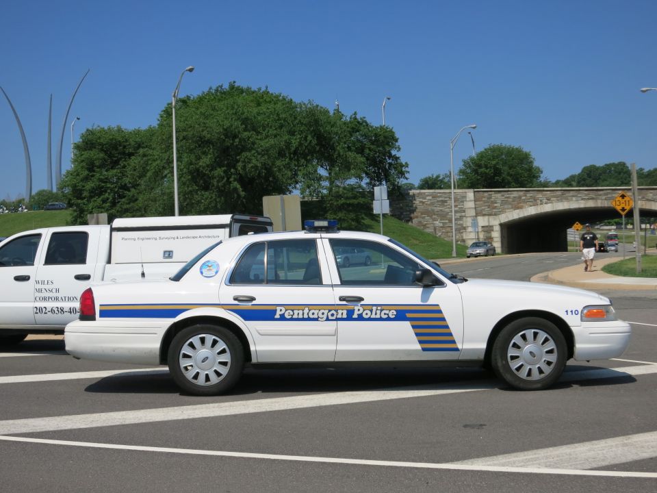 White Pentagon Police sedan in profile beside a marked work van