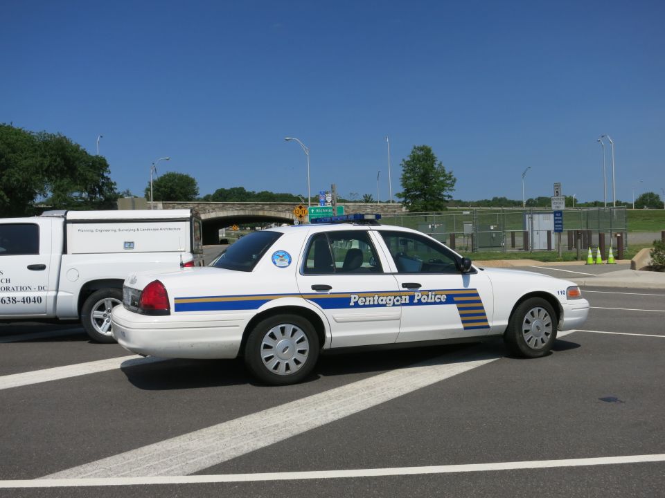 White Pentagon Police sedan, rear three-quarter view near overpass
