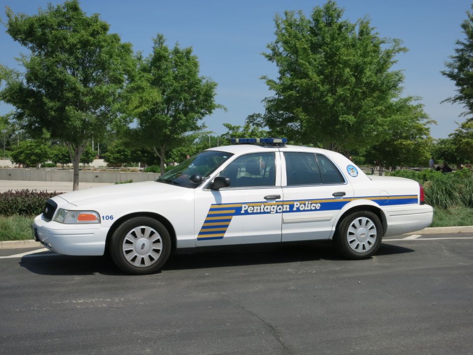White Pentagon Police sedan number 106, front-quarter profile by trees