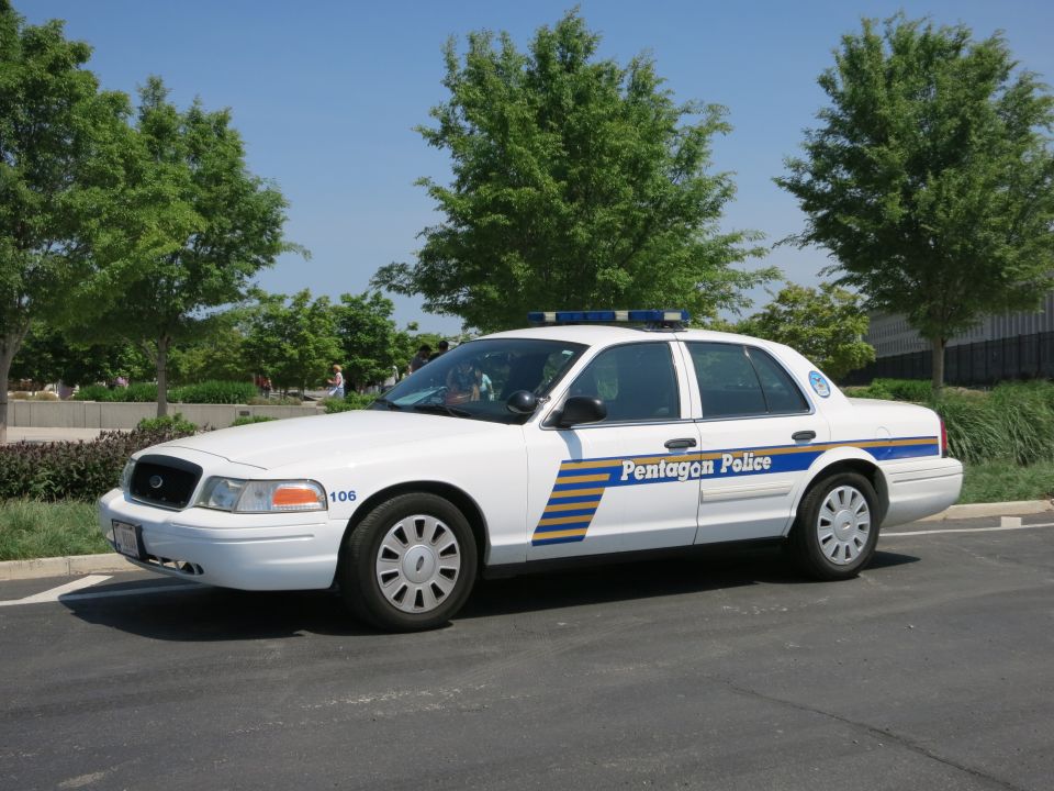 White Pentagon Police sedan number 106, front three-quarter view by trees