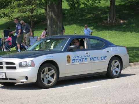 1991 Ford LTD Crown Victoria - silver Dodge Charger lettered Virginia State Police and Trooper drives past spectators seated on a grassy slope.
