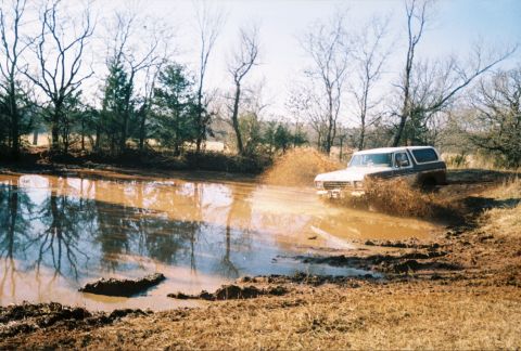 1978 Ford Bronco - A 1978 Ford Bronco navigates a muddy pond, kicking up a large spray of water and dirt.