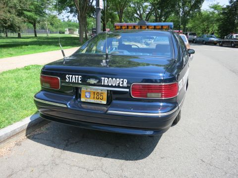 1991 Ford LTD Crown Victoria - Rear view of a dark blue Chevrolet sedan marked STATE TROOPER with a roof light bar and Wisconsin license plate 185.