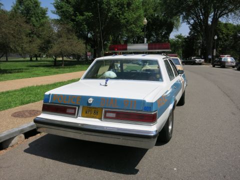 1991 Ford LTD Crown Victoria - Rear of a white-over-blue police sedan lettered POLICE DIAL 911 with unit number 401 and a roof light bar.