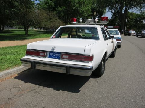 1991 Ford LTD Crown Victoria - Rear view of a white four-door police sedan with red roof lights and license plate 05-21923, parked in a lot.