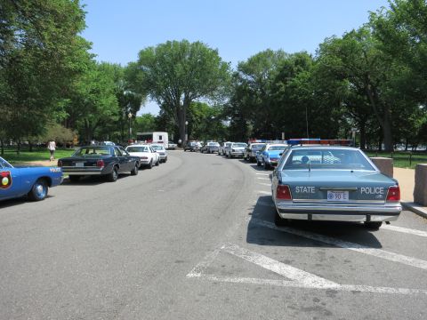 1991 Ford LTD Crown Victoria - long row of marked police cars parked along a tree-lined road, including a State Police sedan in the foreground.