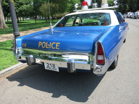 1991 Ford LTD Crown Victoria - Rear view of a blue-and-white police sedan lettered POLICE 218 with chrome bumper and roof light bar, parked on grass.