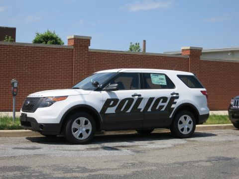 1991 Ford LTD Crown Victoria - white-and-black Ford SUV lettered POLICE on the doors parked along a curb by a low brick wall.