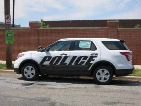 1991 Ford LTD Crown Victoria - Side view of a white-and-black police SUV with large POLICE lettering parked by a brick wall and a parking sign.