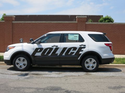 1991 Ford LTD Crown Victoria - Side profile of a white-and-black police SUV with bold POLICE lettering parked along a curb beside a brick wall.