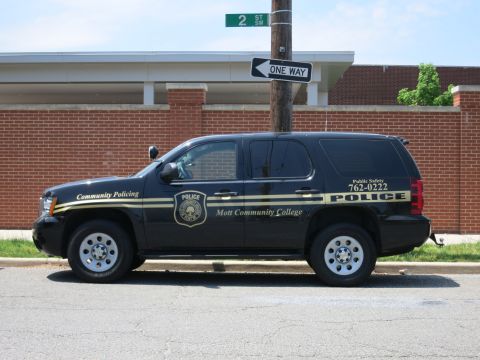 1991 Ford LTD Crown Victoria - black Chevrolet SUV lettered Mott Community College Police parked at a street corner beneath one-way signs.