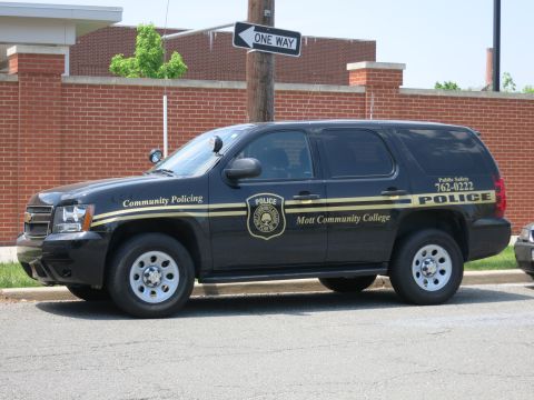 1991 Ford LTD Crown Victoria - Side view of a black Chevrolet campus police SUV lettered Mott Community College Police parked beside a brick wall.