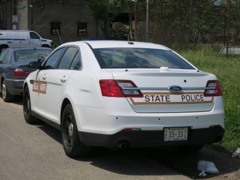 1991 Ford LTD Crown Victoria - Rear view of a white Ford State Police sedan lettered STATE POLICE with Illinois plate 15-33 parked by a fence.