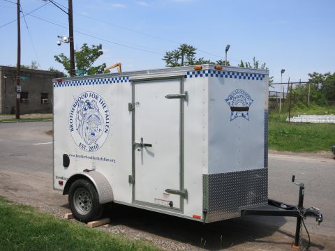 1991 Ford LTD Crown Victoria - small white enclosed cargo trailer parked on gravel, marked with a blue Brotherhood for the Fallen police-memorial emblem.