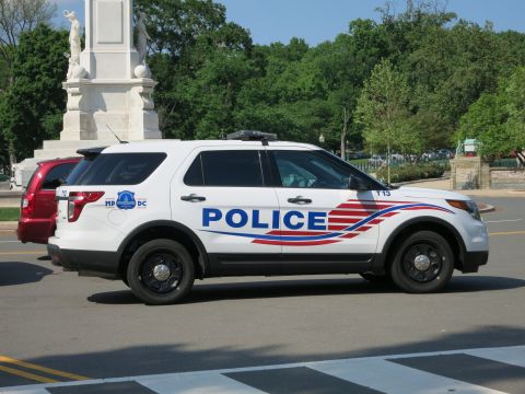 1991 Ford LTD Crown Victoria - white Ford Explorer police SUV with patriotic swoosh graphics and POLICE lettering parked on a road near a monument.