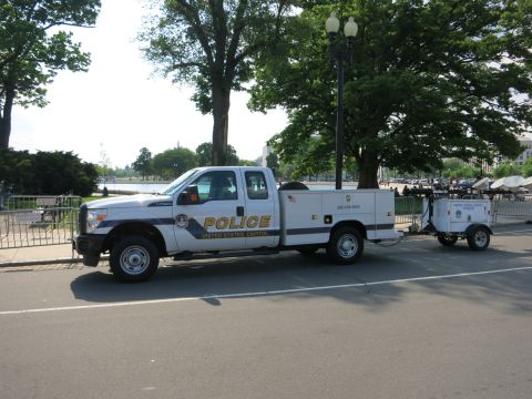 1991 Ford LTD Crown Victoria - white Ford Super Duty Capitol Police utility pickup towing a small trailer, parked along a tree-shaded curb.