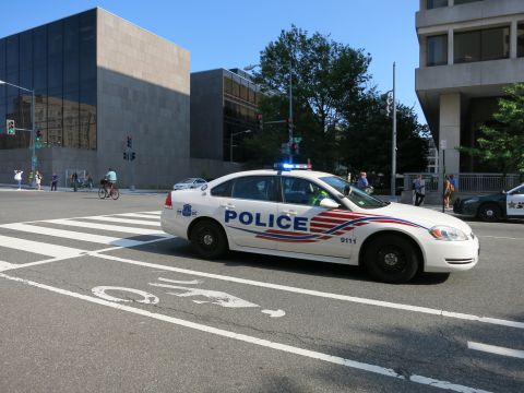 1991 Ford LTD Crown Victoria - white Chevrolet Impala police cruiser with activated lightbar marked POLICE 9111 stopped at a downtown crosswalk.