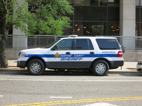 1991 Ford LTD Crown Victoria - white-and-blue Harford County Sheriff Ford Expedition SUV with gold star emblem parked at a downtown curb.