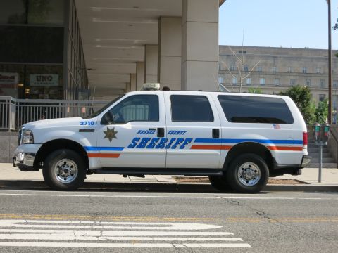 1991 Ford LTD Crown Victoria - white Ford Excursion marked Sheriff 2710 with blue-and-orange striping and a gold star parked along a downtown street.