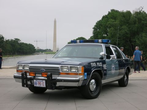 1991 Ford LTD Crown Victoria - vintage blue-and-white Ford LTD Crown Victoria State Police sedan parked on a plaza with the Washington Monument behind.