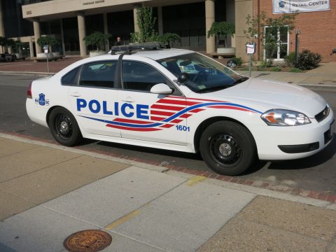 1991 Ford LTD Crown Victoria - white Chevrolet Impala police sedan marked POLICE 1601 parked at a curb outside a Retail Center building.