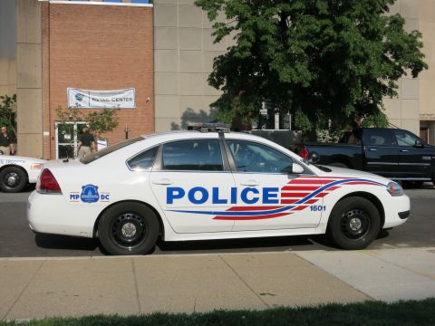 1991 Ford LTD Crown Victoria - white Chevrolet Impala marked POLICE MPDC 1601 parked at a curb beside a black pickup outside a brick building.