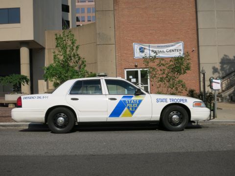 1991 Ford LTD Crown Victoria - white Ford Crown Victoria marked New Jersey State Police State Trooper with blue-and-yellow door emblem parked by a brick building.