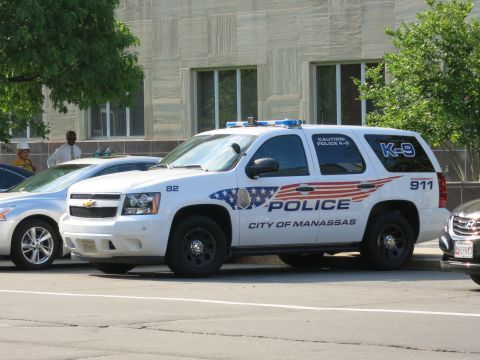 1991 Ford LTD Crown Victoria - white Chevrolet Tahoe marked City of Manassas Police K-9 with American-flag graphics sits parked on a downtown street.