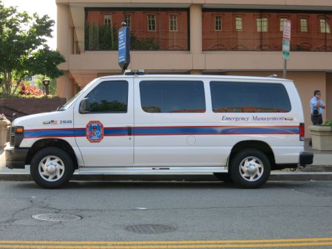 1991 Ford LTD Crown Victoria - Side view of a white Ford E-Series Emergency Management van parked on a street, with a person standing on the sidewalk.