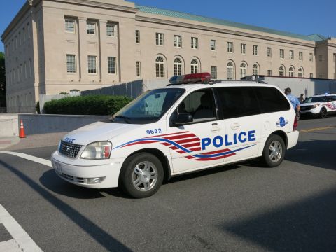 1991 Ford LTD Crown Victoria - white Ford Freestar minivan marked Police with red, white and blue stripe graphics parked on a street near a stone building.