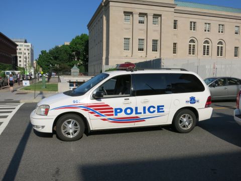 1991 Ford LTD Crown Victoria - white Police minivan with red, white and blue stripe graphics is parked at a crosswalk in front of a large stone building.