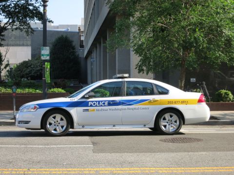 1991 Ford LTD Crown Victoria - Side view of a white Chevrolet Impala marked MedStar Washington Hospital Center Police parked along a curb with trees behind.