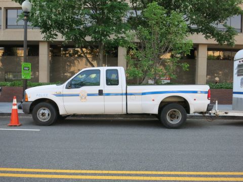 1991 Ford LTD Crown Victoria - white Ford dually Police pickup truck with blue striping is parked at the curb near an orange traffic cone.