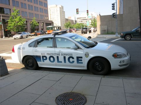 1991 Ford LTD Crown Victoria - Side view of a white D.C. Protective Services police sedan unit 419 parked along a downtown curb with traffic behind.