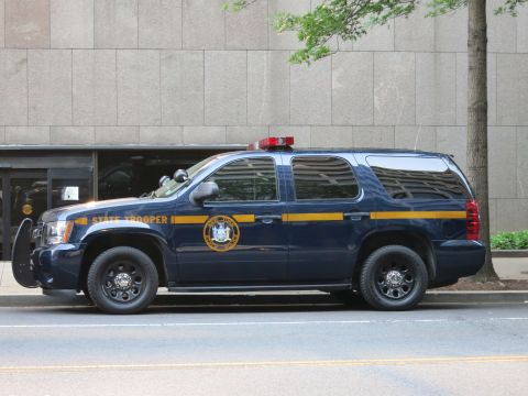 1991 Ford LTD Crown Victoria - Side view of a dark blue State Trooper SUV with gold stripe and agency seal parked along an urban street.