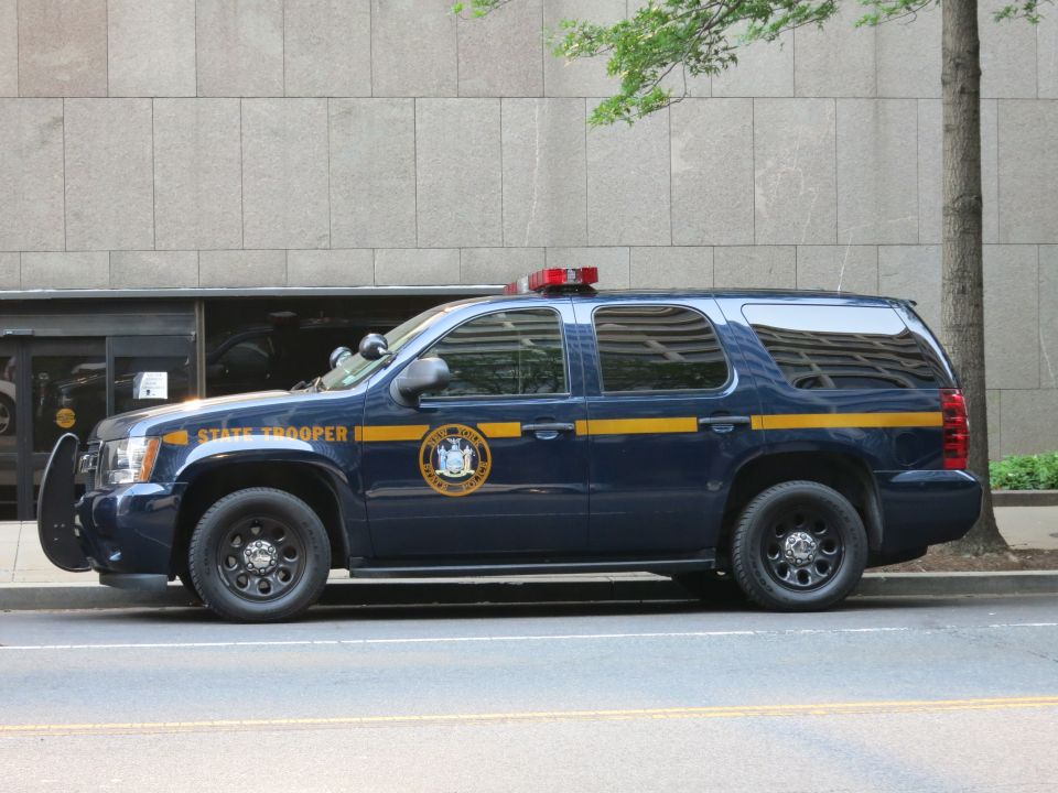 Dark blue State Trooper SUV with gold stripe parked curbside