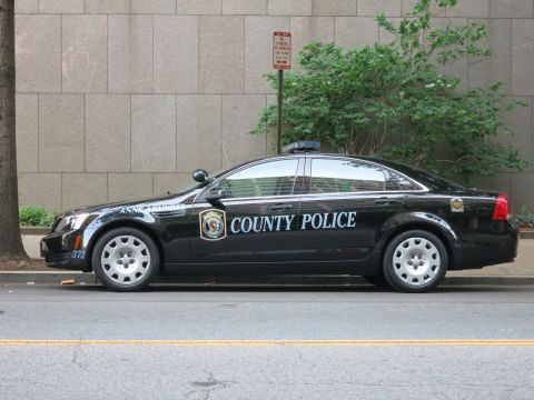 1991 Ford LTD Crown Victoria - Side view of a black County Police sedan with chrome wheels and unit 372 parked along a city street.