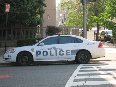 1991 Ford LTD Crown Victoria - white D.C. Protective Services police sedan unit 419 sits at an intersection as a pedestrian crosses behind it.