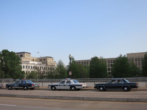 1991 Ford LTD Crown Victoria - Three vintage sedans, including a Boston Police cruiser, lined up on a bridge before city buildings.