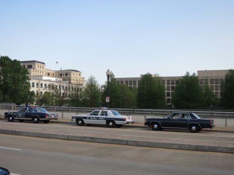 1991 Ford LTD Crown Victoria - Three vintage sedans, one a Boston Police cruiser, parked along a bridge with buildings and trees behind.