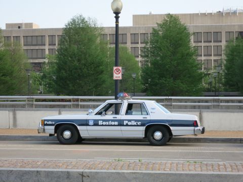 1991 Ford LTD Crown Victoria - white-and-blue Boston Police sedan unit 7087 parked on a bridge beside a no-parking sign and lamppost.